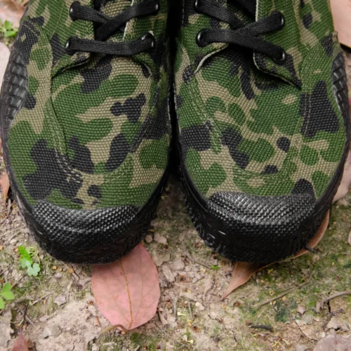Close-up view of the front part of camouflage training shoes, showing reinforced stitching and textured rubber toe protection.