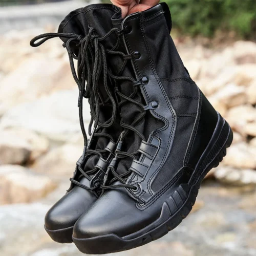 Pair of black combat boots held by hand, featuring abrasion-resistant leather and high ankle support for military professionals.