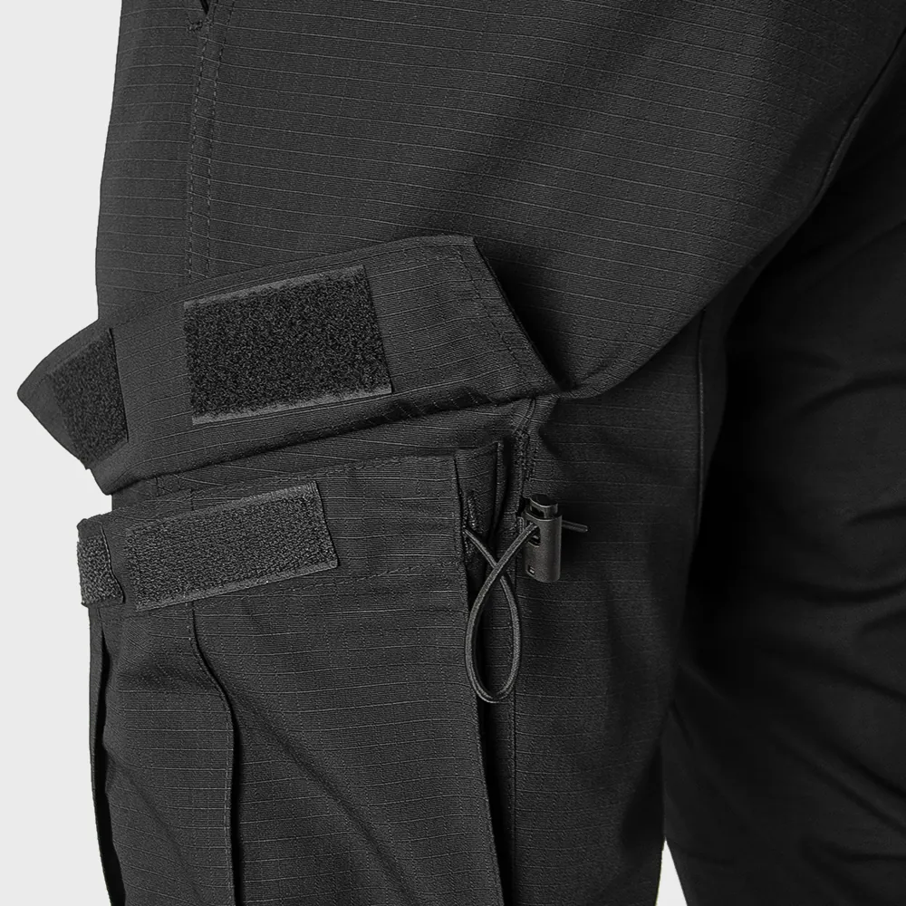 Cargo pocket construction detail with hook-and-loop closures on black tactical trousers. Customization can include pocket dimensions, closure style, reinforcement stitching, and accessory attachment options.