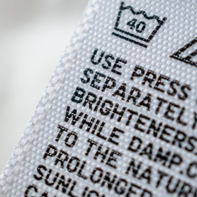 Detail view of a care label showing washable instructions and compliance markings. OEM program support includes label layout, language options, and printing coordination for bulk production.